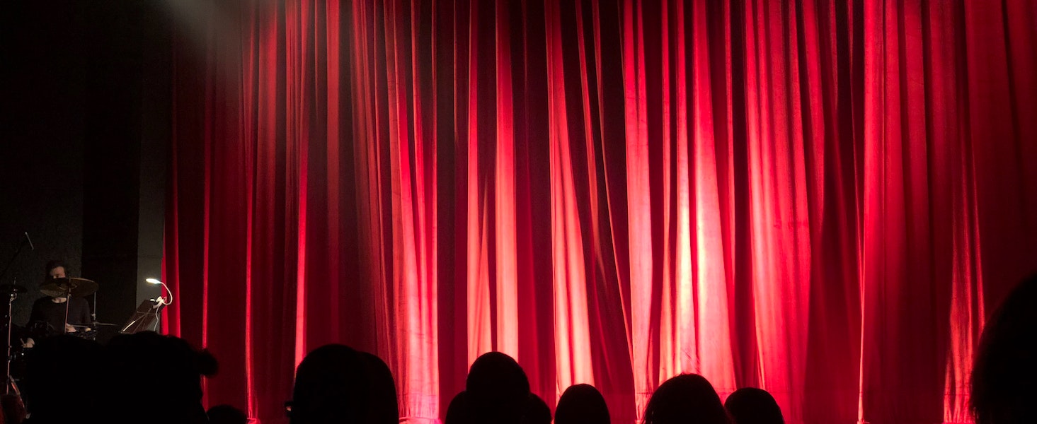 A crowd of people sitting waiting to see a show behind a red curtain